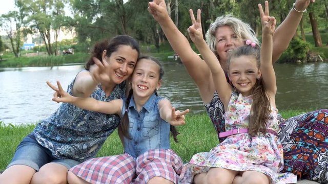 Two happy mothers with two small children play and have fun sitting in the Park on the lawn at sunset. Close up. 4K, 29.97 fps.