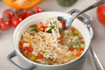 Fresh vegetable soup with noodles in spoon over dish, closeup. Diet food