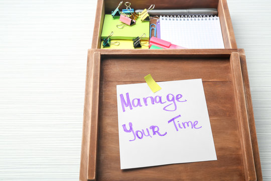 Wooden box with written phrase "Manage your time" on paper sheet and stationery on table. Time management concept
