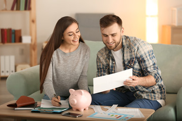Happy couple with pay bills, calculator and money counting expenses indoors. Money savings concept