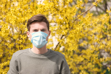 Young man in protective mask near blooming tree. Allergy concept