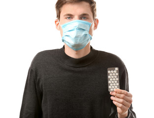 Young man in protective mask holding pills on white background. Allergy concept