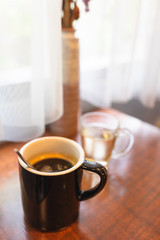 Americano coffee on wooden table near window with sunlight.