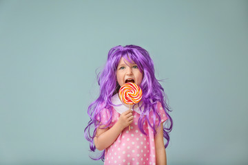 Cute little girl in purple wig and with lollipop on color background