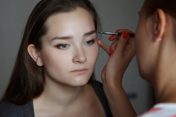 The make-up master models the shape of the eyebrows on the face of a young, beautiful girl.