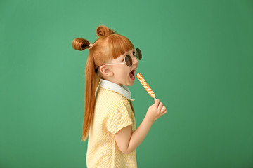 Cute little girl with lollipop on color background