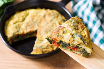 Frittata made of eggs and vegetables in a iron pan, on wooden table. 