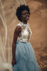 Black bride in beautiful wedding dress and bridal veil stands and smiles.
