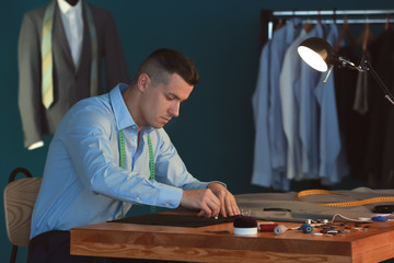 Young tailor marking fabric with chalk in atelier