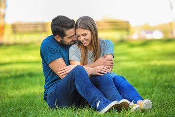Happy young couple sitting on green lawn in park