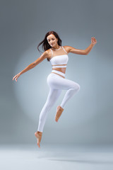 Fototapeta premium Attractive excited fitness girl, ballerina dancer in sportwear jumping of joy isolated over gray background.