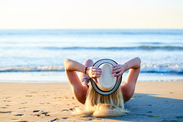 Mujer tumbada en la arena de la playa con sombrero de paja