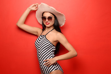 Naklejka premium Beautiful young woman in swimming suit with sunglasses and hat on color background