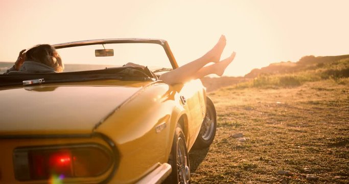Young women relaxing in convertible car and looking at sunset