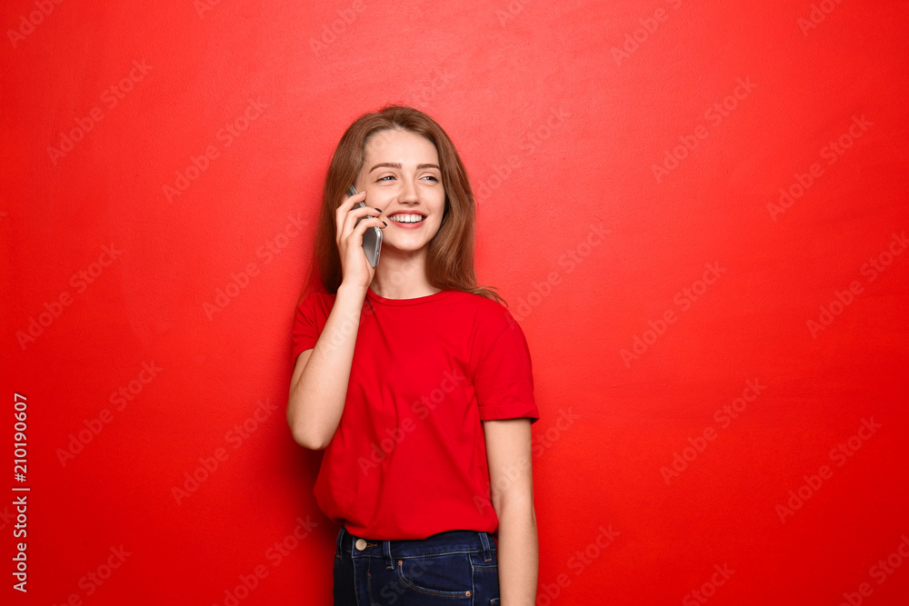 Wall mural beautiful young woman talking on mobile phone against color background