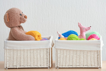 Wicker baskets with balls of knitting yarn and funny toys on table against light background