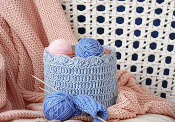 Fototapeta na wymiar Basket with balls of knitting yarn and unfinished clothes in armchair
