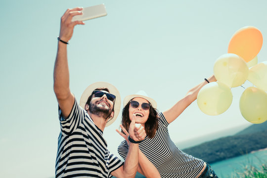 Smiling couple wearing sunglasses with balloons make selfie photo over sea background