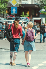 back view of young couple with backpacks walking in city