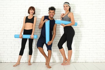 Fototapeta premium Group of sporty people with yoga mats near white brick wall