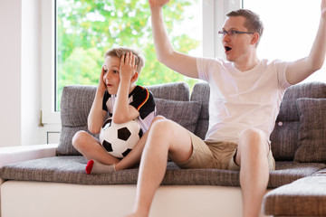 Young father and his son watching world soccer championship with ball on