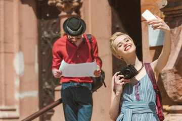 girl with camera taking selfie on smartphone while man lookoing at map