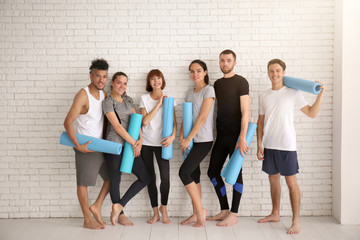 Fototapeta na wymiar Group of sporty people with yoga mats near white brick wall