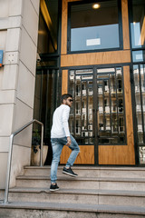 A young man travels through the streets of the city. Boy in sunglasses Stylish man near the building. The man sits on a whip. Beard and hair in a stylish guy.