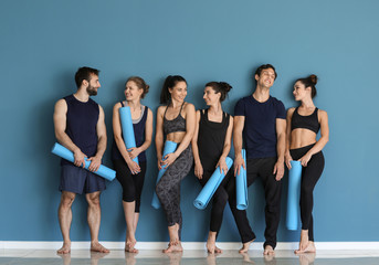 Fototapeta na wymiar Group of people with yoga mats near color wall