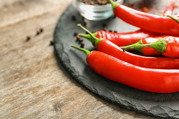 Slate plate with fresh chili peppers on wooden background, closeup
