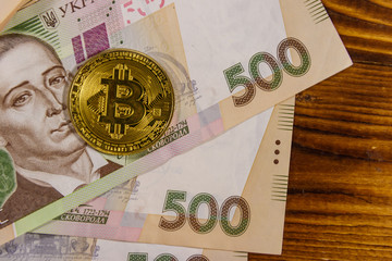 Golden bitcoin and five hundred ukrainian hryvnia bills on wooden background