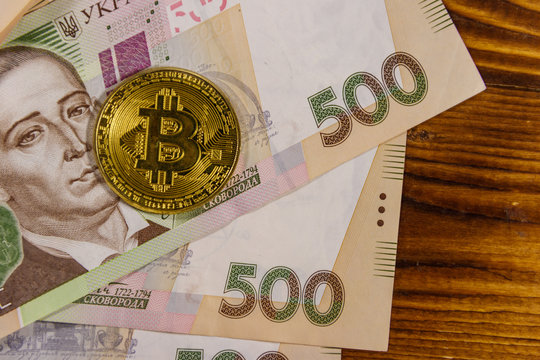 Golden bitcoin and five hundred ukrainian hryvnia bills on wooden background