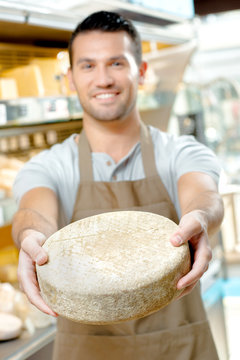 Shop worker holding circular cheese in outstretched arms