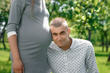 Happy pregnant woman, family couple in the park, green floral background. In anticipation of a miracle, a child. Family life, children, pregnancy, family, father, mother. Copy space