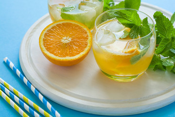 Orange lemonade with slices of orange, ice and mint on blue background.