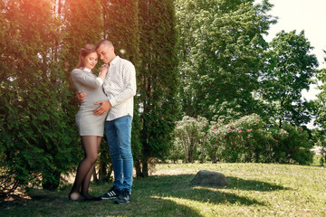 Fototapeta premium Happy pregnant woman, family couple in the park, green floral background. In anticipation of a miracle, a child. Family life, children, pregnancy, family, father, mother. Copy space
