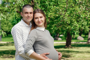 Happy pregnant woman, family couple in the park, green floral background. In anticipation of a miracle, a child. Family life, children, pregnancy, family, father, mother. Copy space