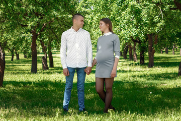 Obraz premium Happy pregnant woman, family couple in the park, green floral background. In anticipation of a miracle, a child. Family life, children, pregnancy, family, father, mother. Copy space