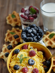 Tasty cornflakes with raspberries and blueberries on blue background. Wafers and milk.
