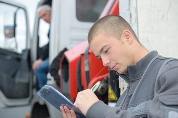 driver writing on clipboar next to trucks and trailers