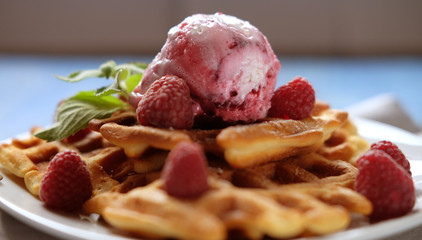 Waffles with raspberry ice cream and fresh raspberries, decorated with mint over blue wooden background