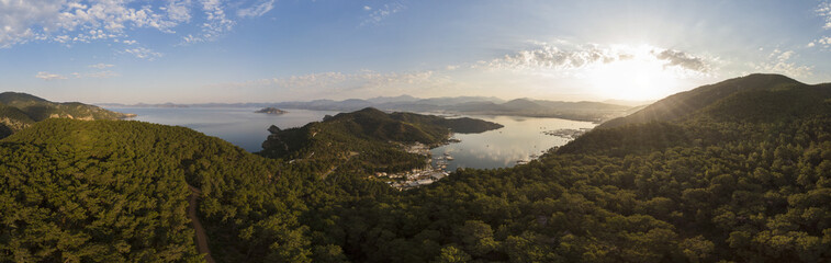 Fototapeta na wymiar Aerial over a small harbour town surrounded by mountains and forest at sunrise, Fethiye, Turkey