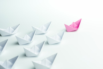 Woman leadership concept with pink paper ship leading among white on white background.