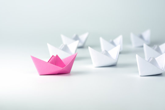 Woman Leadership concept with pink paper ship leading among white on white background.