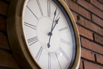 Side close-up of a wooden classic and simple wall clock hanging in a red brick wall by a rope. It...