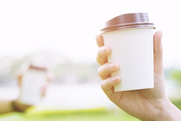 two hand holding paper cup of take away drinking coffee on natural morning sunlight. space Place...