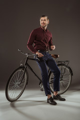 full length view of handsome smiling young man sitting on bicycle and looking away on black