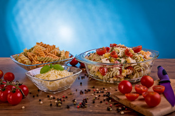 Delicious pasta salad or Mediterranean salad. Tomatoes mozzarella basil corn spice and olive oil on a wooden table. Traditional Italian food
