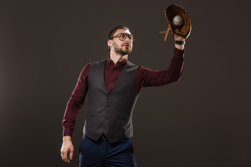 concentrated businessman in eyeglasses catching baseball ball with glove isolated on black