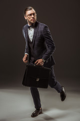 serious businessman with briefcase running and looking away on black